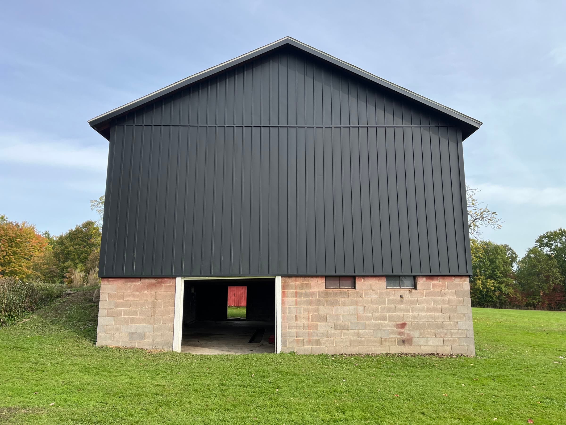 Completed barn gable with charcoal vertical metal siding over a concrete block base